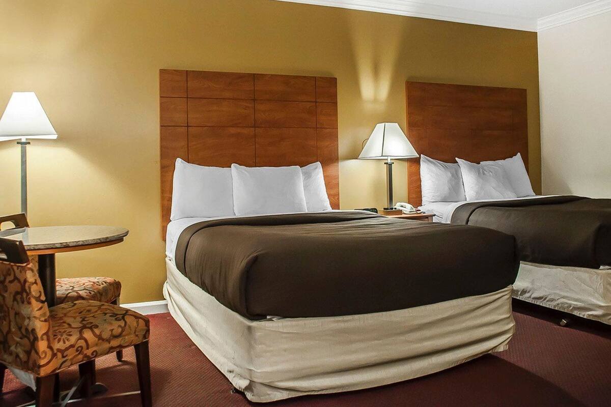 A hotel room with two beds, a small table with a chair, and two bedside lamps.