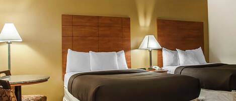 A hotel room with two beds, a small table with a chair, and two bedside lamps.