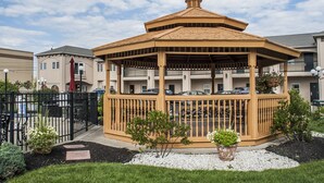 Ein Pavillon mit Holzdach und Geländern, umgeben von einem schwarzen Zaun und Blumentöpfen.