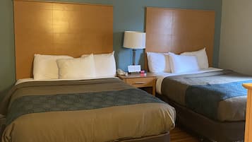 A hotel room with two beds, wooden headboards, a nightstand with a lamp, and a wooden floor.