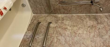 A bathroom with a bathtub, a shower with a handheld showerhead, and two grab bars on the floor.