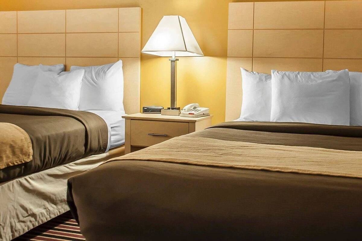 A hotel room with two beds, a nightstand with a lamp, and a telephone.
