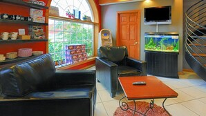 Ein Wohnzimmer mit einem schwarzen Ledersofa, einem roten Couchtisch, einem Aquarium, einem Fernseher und einer Wendeltreppe.