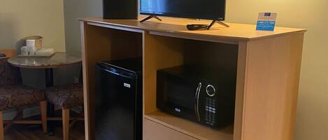 A compact kitchenette with a refrigerator, microwave, and a flat-screen TV on a wooden cabinet.