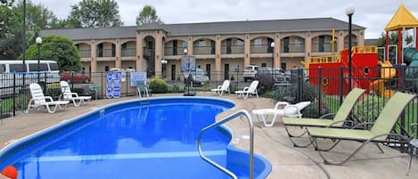 A swimming pool with lounge chairs, a children's play area, and a building with multiple balconies in the background.