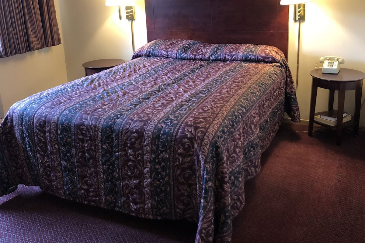 A hotel room with a large bed, two bedside lamps, a framed picture on the wall, and a telephone on a bedside table.