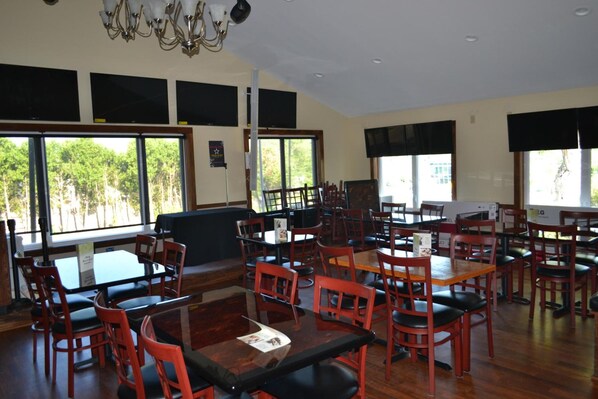 A restaurant with multiple tables and chairs, large windows with a view of trees, and a chandelier.
