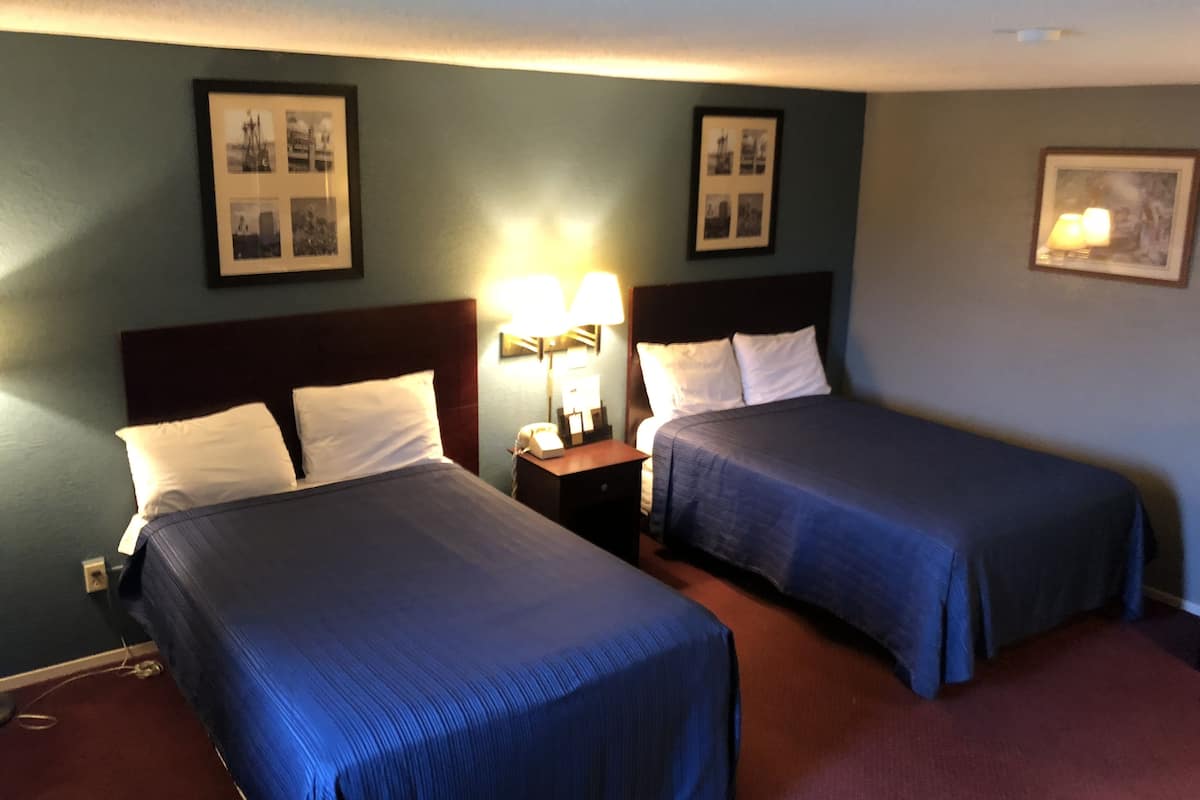 A hotel room with two beds, a nightstand with a lamp, and framed pictures on the walls.