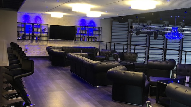 A modern lounge area with leather sofas and chairs, a bar with shelves, and a large flat-screen TV. - Latham Inn (Latham)