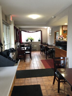 A restaurant with a counter, tables, chairs, and a view of the outside through a window.