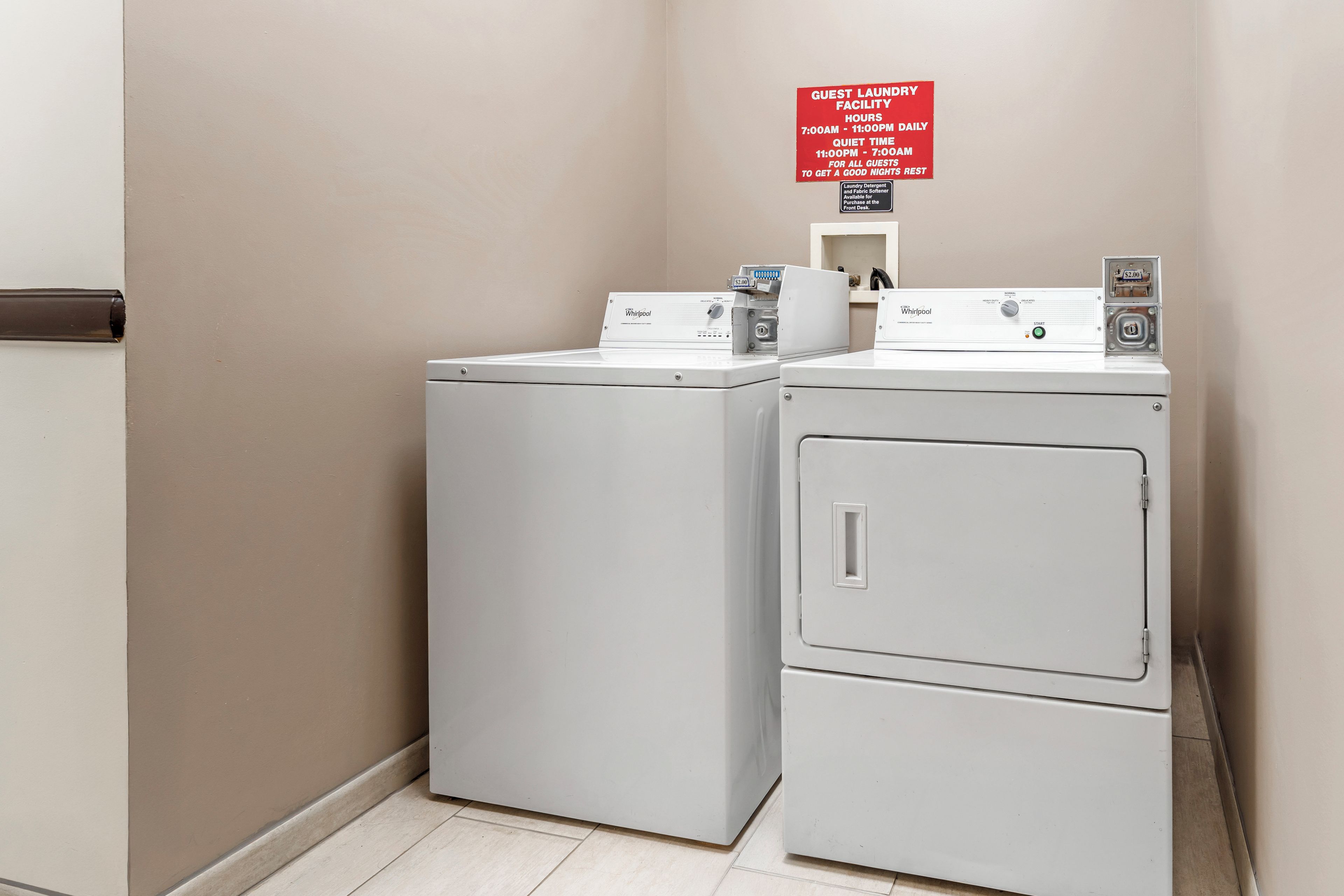 A laundry facility with two Whirlpool washers and a sign indicating guest laundry hours and quiet time.