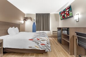 Ein Hotelzimmer mit einem Bett, einem Schreibtisch, einer Mikrowelle, einem Kühlschrank und einem flachbildschirmfernseher an der Wand.
