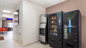 Máquina de vendas com lanches e bebidas, um bebedouro e uma placa fixada na parede.