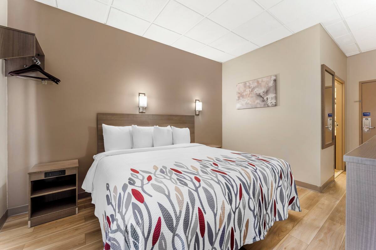 Ein Hotelzimmer mit einem Bett, Nachttischen, einem Wand-Fernseher und einem Gemälde.