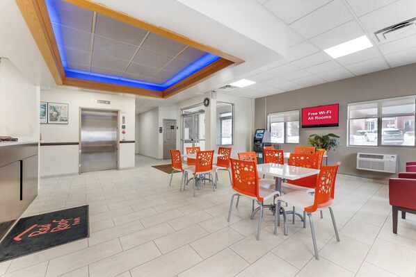 Un espace de salle à manger moderne avec une table centrale, des chaises orange et un plafond doté d’un éclairage bleu.