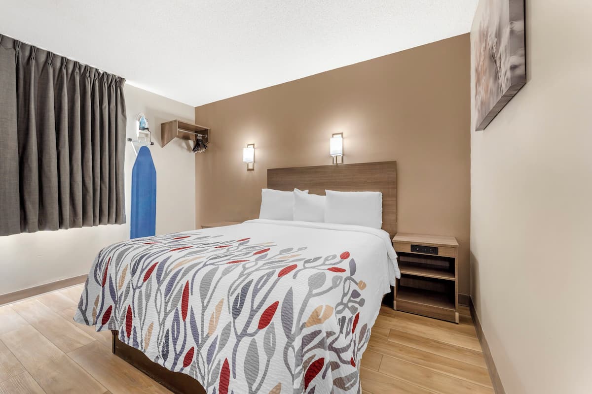 Ein Hotelzimmer mit Bett, Nachttisch, einer Wandablage und einem Fenster mit Vorhängen.