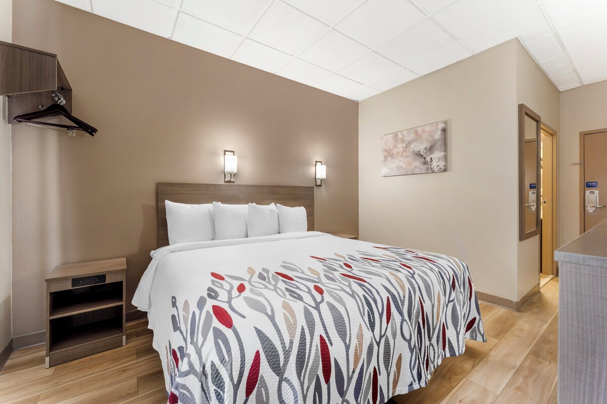 A hotel room with a bed, bedside tables, a wall-mounted TV, and a painting.