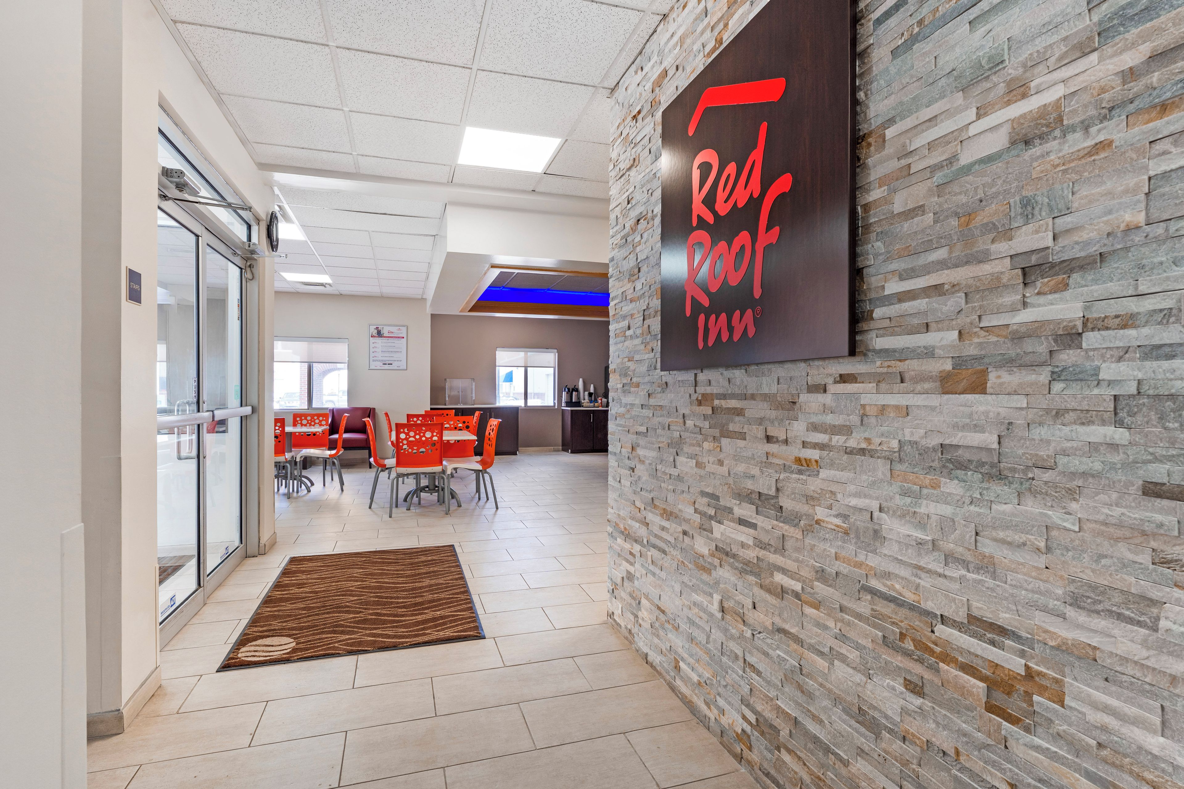 A Red Roof Inn lobby with a stone wall, a reception desk, and a seating area with orange chairs.