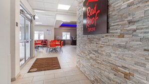 De lobby van een Red Roof Inn, met een stenen muur, een receptiebalie en een zithoek met oranje stoelen.