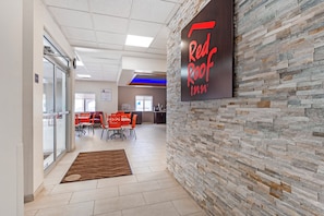 A Red Roof Inn lobby with a stone wall, a reception desk, and a seating area with orange chairs.