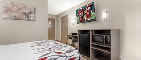 A hotel room with a bed, a TV, a microwave, and a desk.