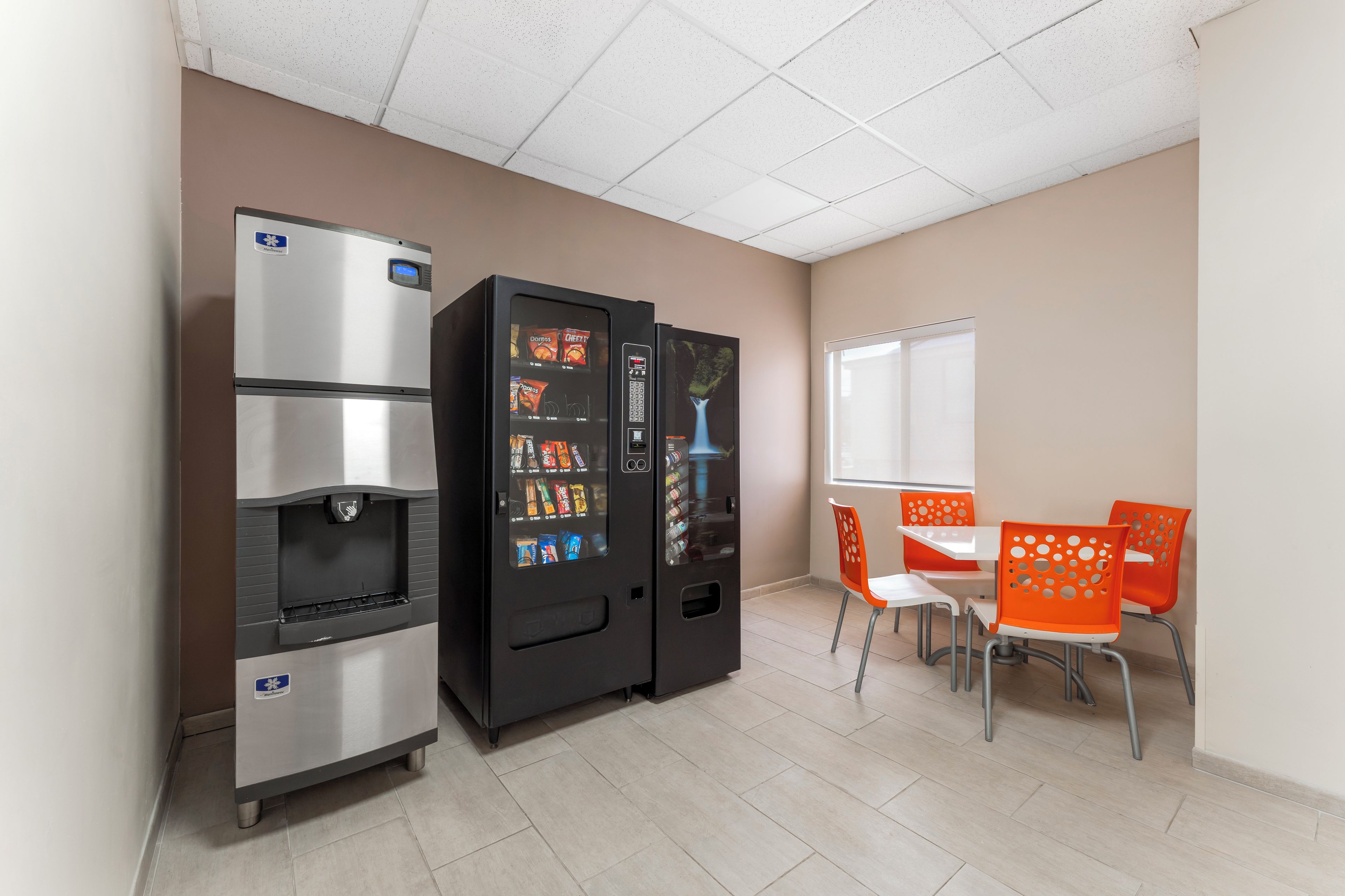 A room with a vending machine, a refrigerator, and a table with chairs.