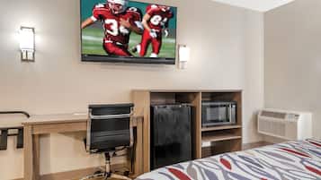 Habitación de hotel con cama, escritorio con silla, televisor montado en la pared y aire acondicionado integrado.