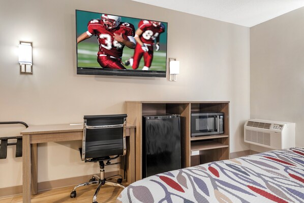 Habitación de hotel con cama, escritorio con silla, televisor montado en la pared y aire acondicionado integrado.