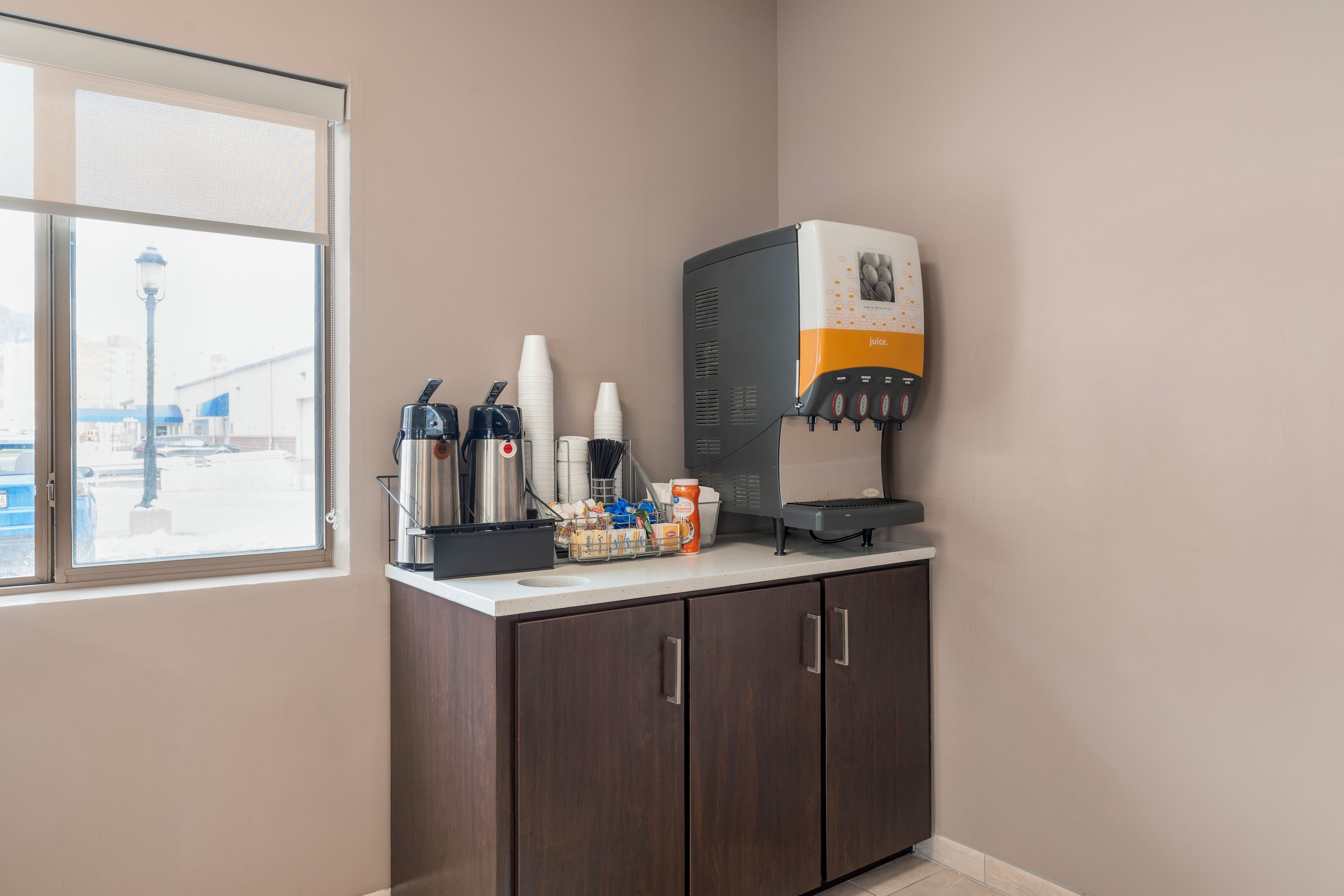 A coffee station with a coffee machine, cups, and a juice dispenser.