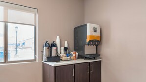 Een koffiehoek met een koffieapparaat, bekers en een sapautomaat.