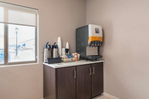 A coffee station with a coffee machine, cups, and a juice dispenser.