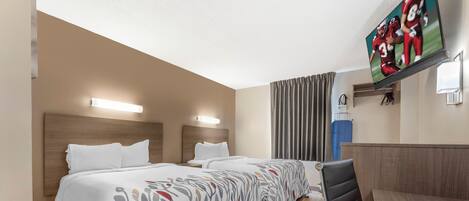 Habitación de hotel con dos camas, un escritorio, una silla y un televisor en la pared.