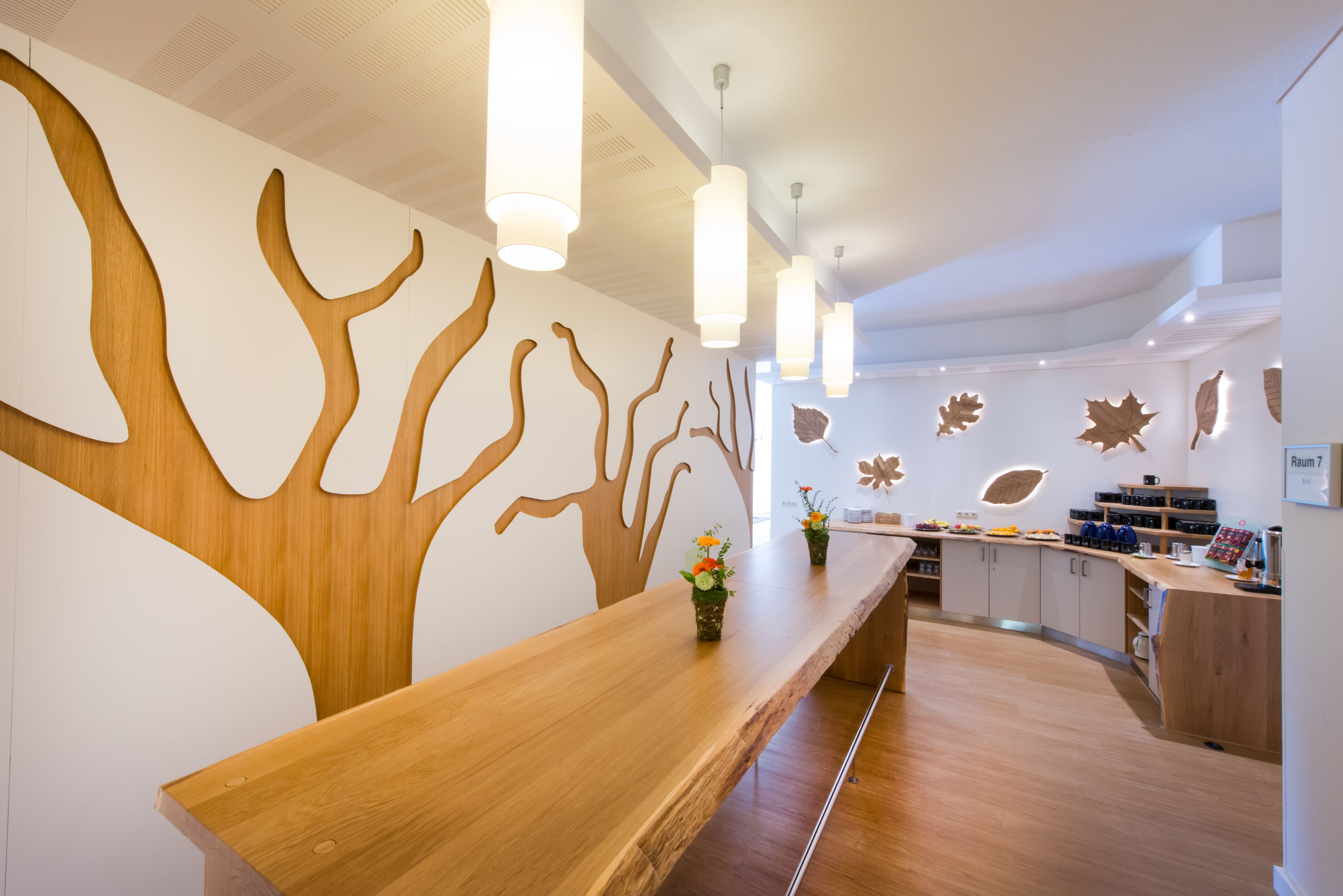 A modern reception area with a wooden reception desk, pendant lighting, and a wall with abstract tree-like designs.