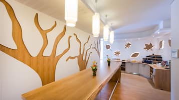 A modern reception area with a wooden reception desk, pendant lighting, and a wall with abstract tree-like designs.