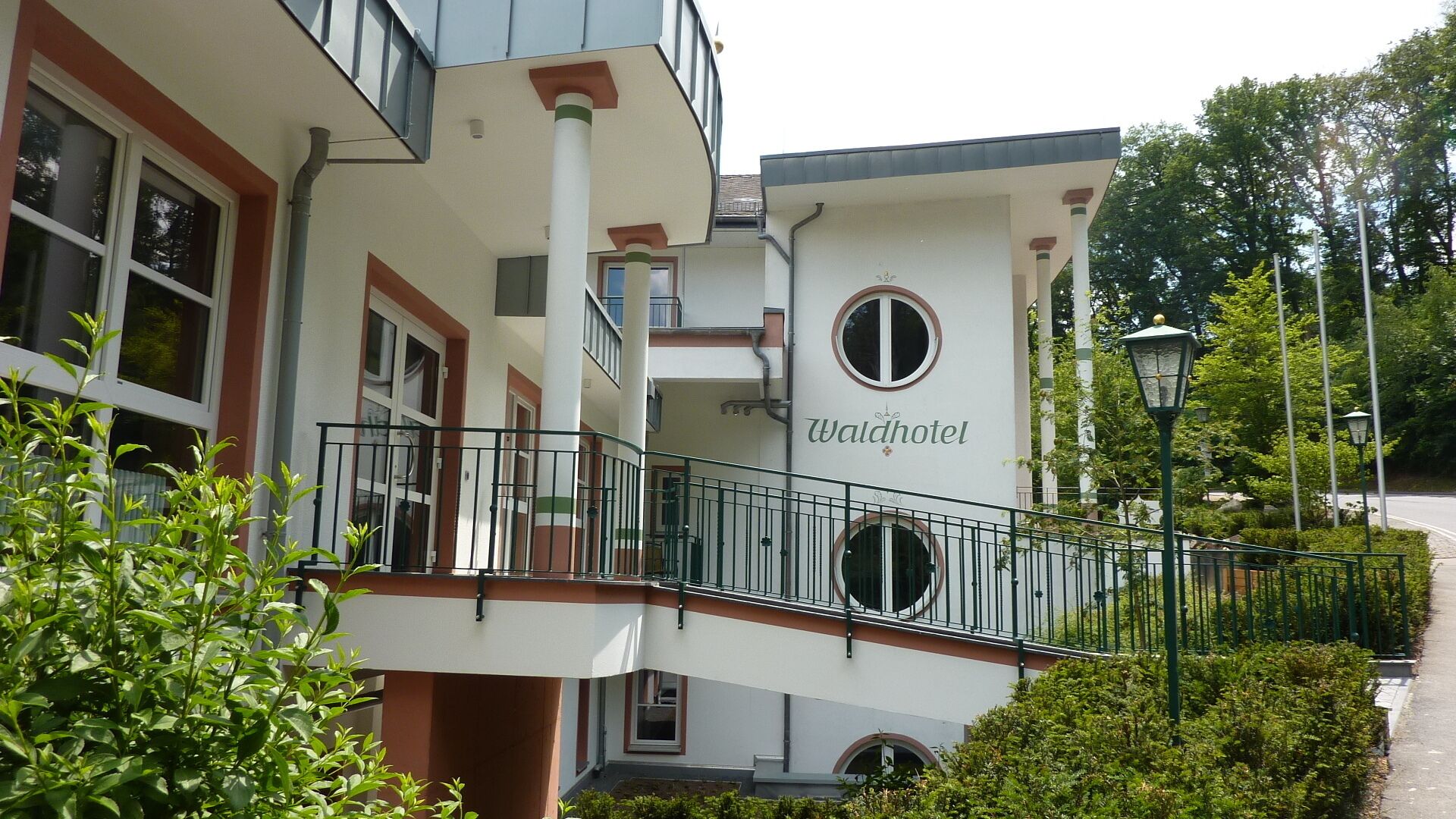 Ein Hotel mit Balkon, einem Schild mit der Aufschrift 'Waldhotel' und einem Weg zum Eingang.