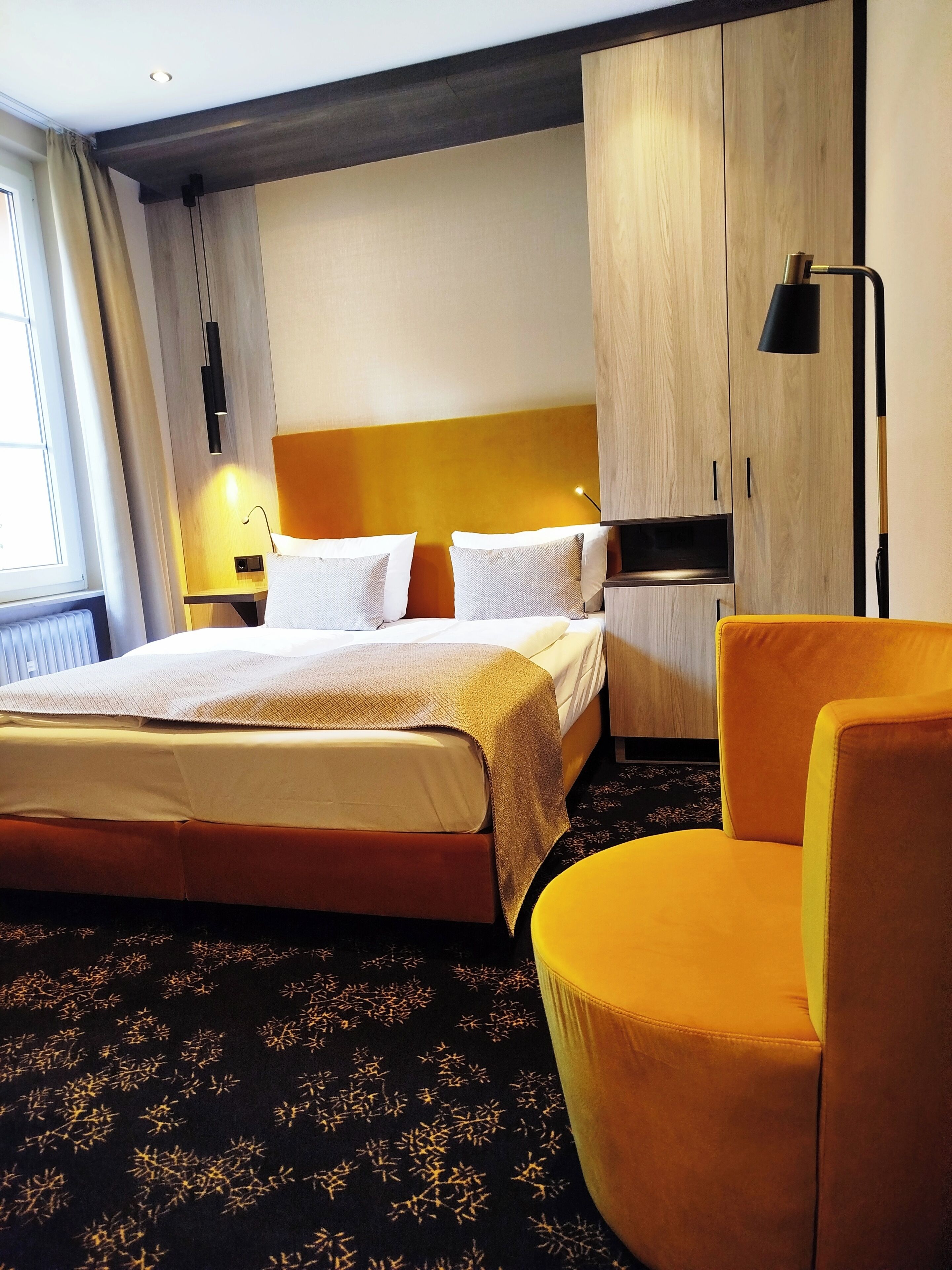 Una habitación de hotel con una cama grande, una mesita de noche, una silla y un armario.