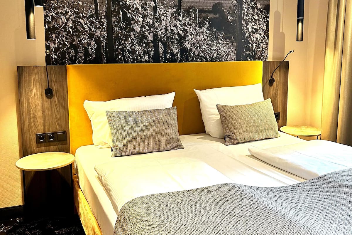 A hotel room with a large bed, two bedside tables, a wall-mounted TV, and a view of a cityscape.