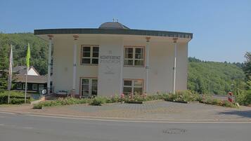 A building labeled "Konferenzzentrum Zentrums" with a flat roof, large windows, and a paved entrance area with flower beds.