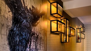 Um corredor com uma grande escultura de árvore, iluminação moderna embutida na parede e uma fileira de cadeiras cinzas estofadas.