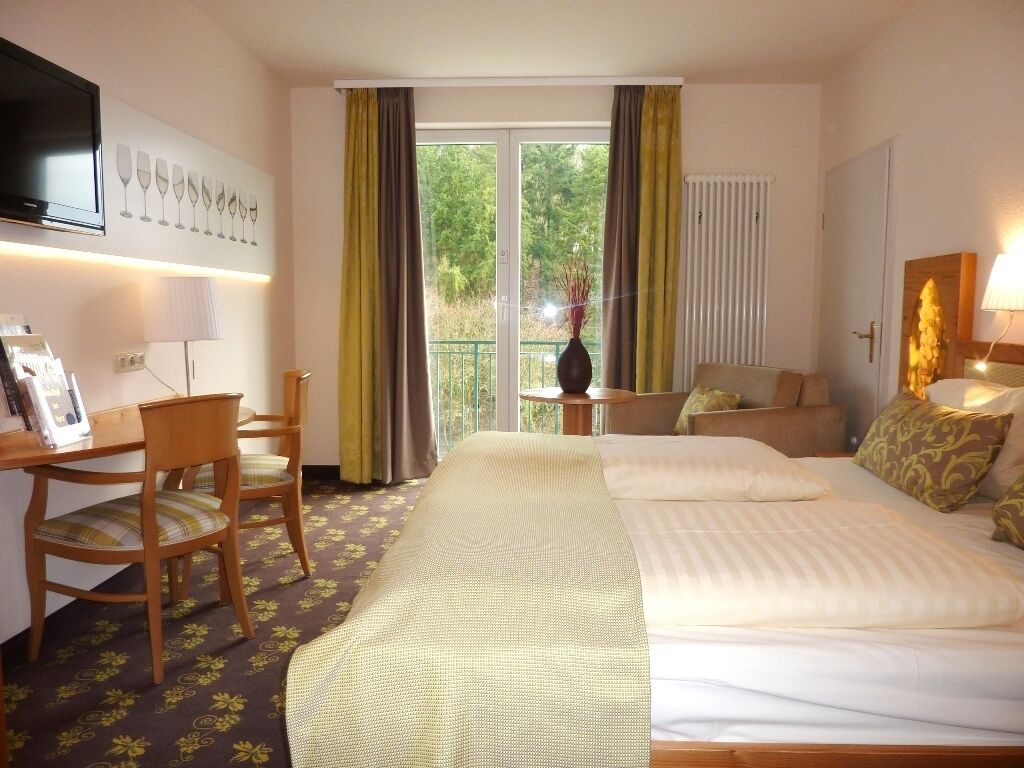 Una habitación de hotel con cama, escritorio, silla, televisor y ventana con cortinas.