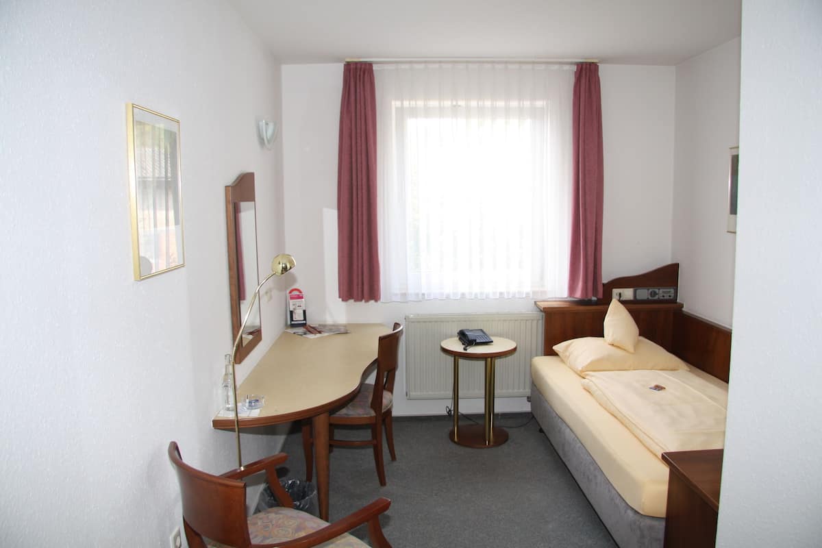 Een hotelkamer met een bed, een bureau, een stoel, een klein tafeltje, een spiegel en een raam met gordijnen.