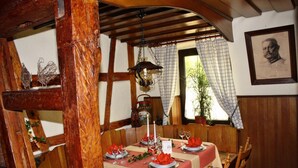 A dining area with wooden beams, a chandelier, and a table set for two with red napkins and glasses.