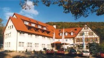 A large building with a red roof and multiple windows, surrounded by parked cars and trees.