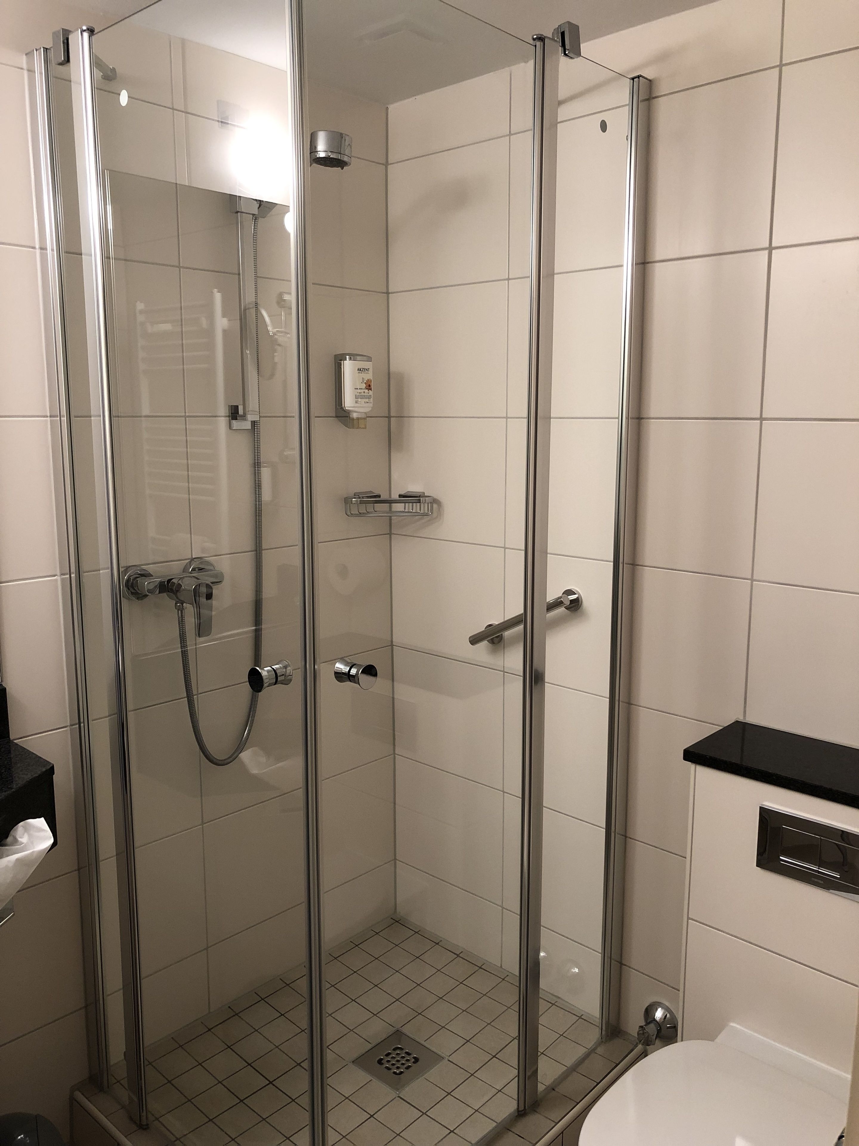 Douchecabine met glazen wanden, een handdouche, een douchehouder en een zeepdispenser op de muur.