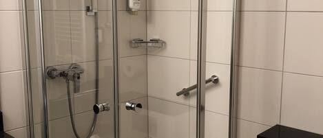 Douchecabine met glazen wanden, een handdouche, een douchehouder en een zeepdispenser op de muur.