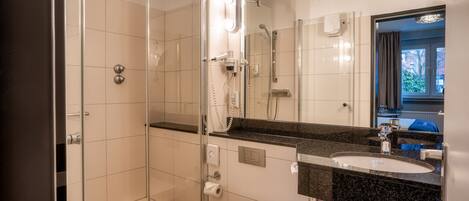 A modern bathroom with a glass-enclosed shower, a white toilet, a sink with a black countertop, and a large mirror.