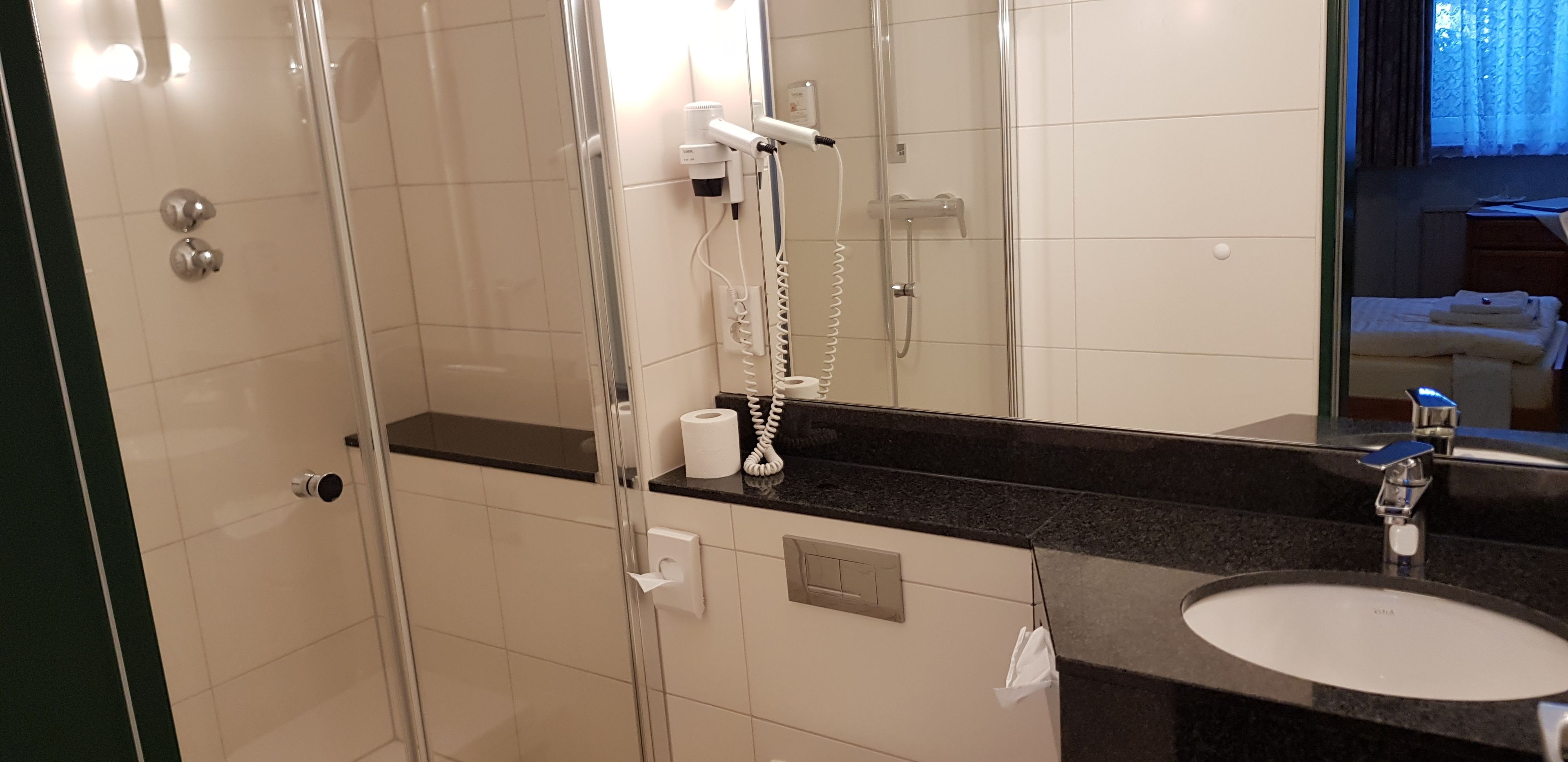 A modern bathroom with a glass shower enclosure, a black countertop, a sink, and a mirror.