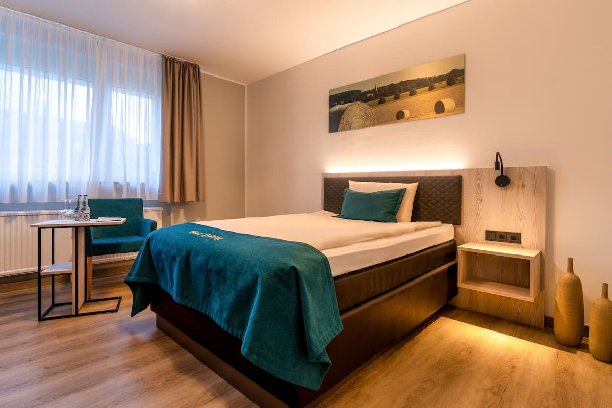 Quarto de hotel moderno com uma cama, uma escrivaninha, uma cadeira e um quadro na parede.