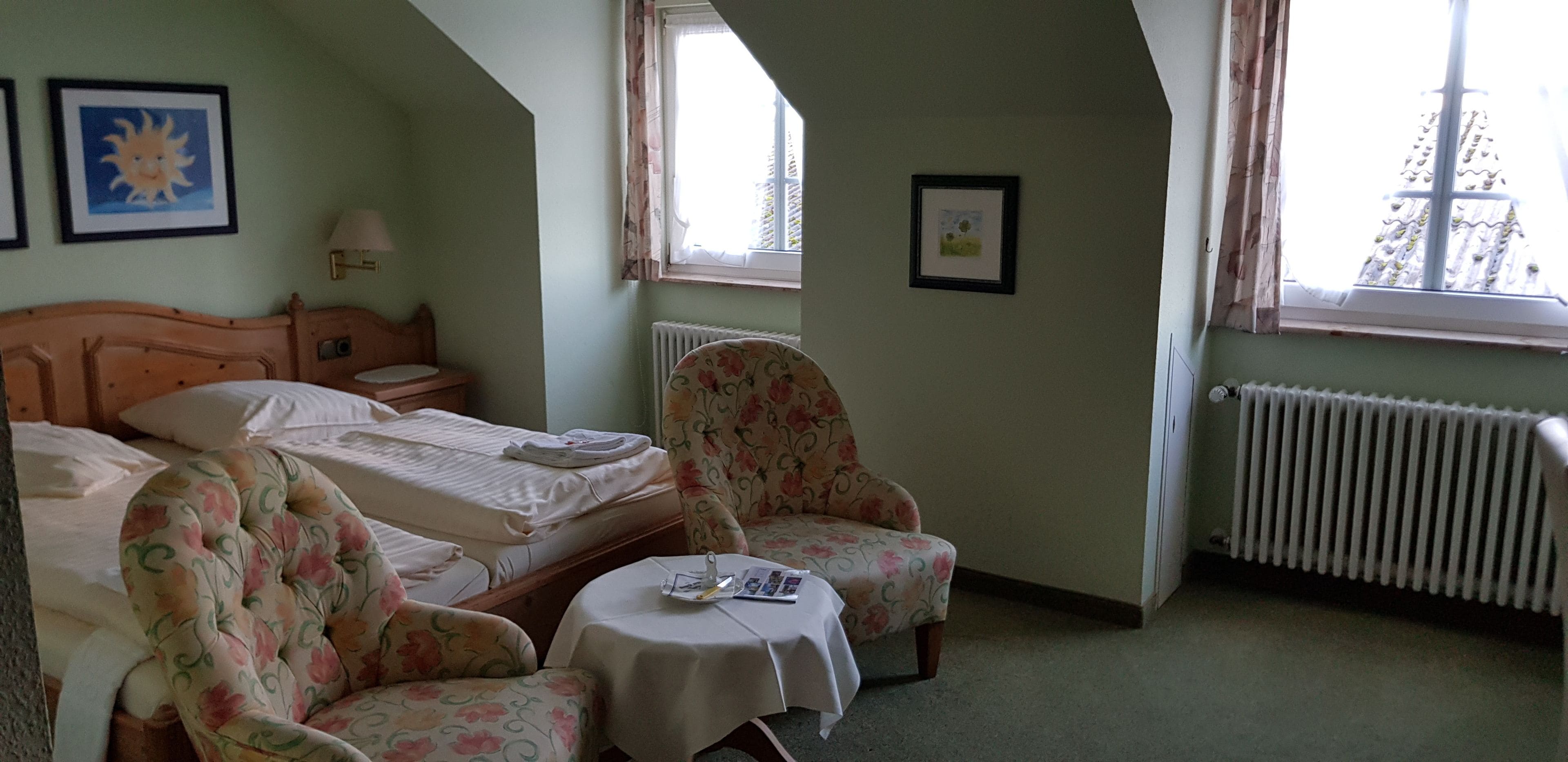 A bedroom with two beds, a chair, a small table, and a radiator.