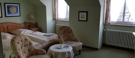 Een slaapkamer met twee bedden, een stoel, een klein tafeltje en een radiator.